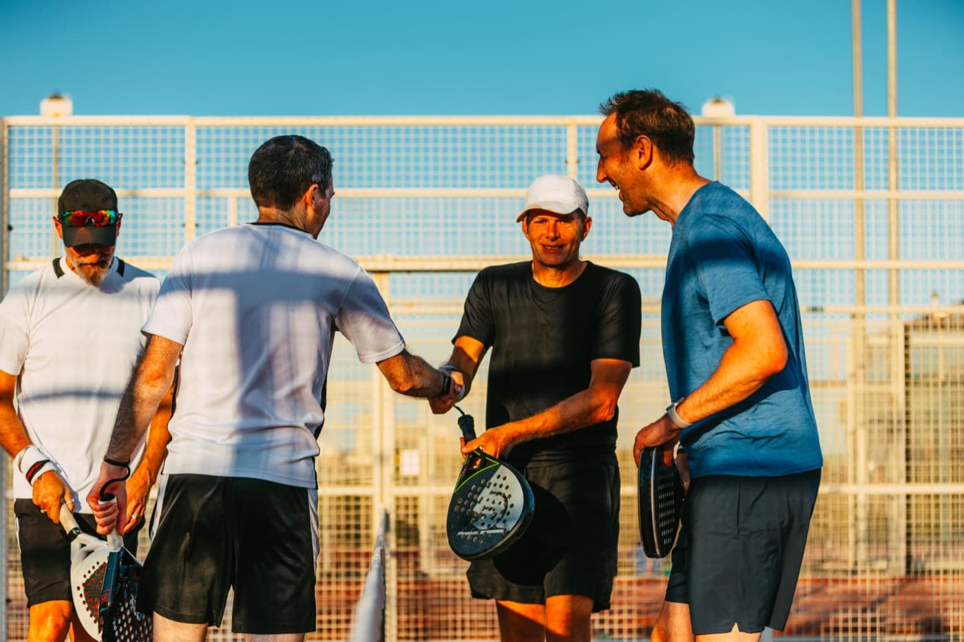 Four padel players shaking hands over the net after a match